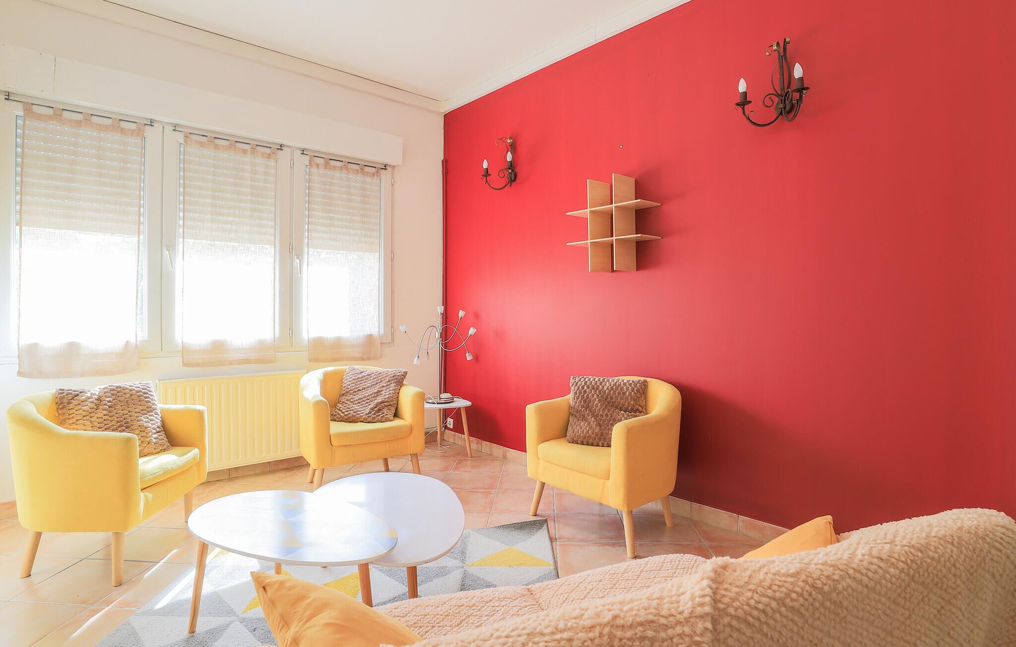 Un salon avec des fauteuils jaunes, une table basse ronde et un mur d’accent rouge.