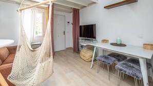 A modern living space with a hanging hammock, a sofa, a dining table, a TV, and a small kitchenette. - GuestReady - Confy Flat in Madrid (Madrid)