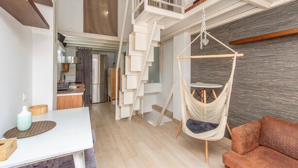 A modern interior with a staircase leading to a loft area, a hanging chair, and a cozy seating area. - GuestReady - Confy Flat in Madrid (Madrid)
