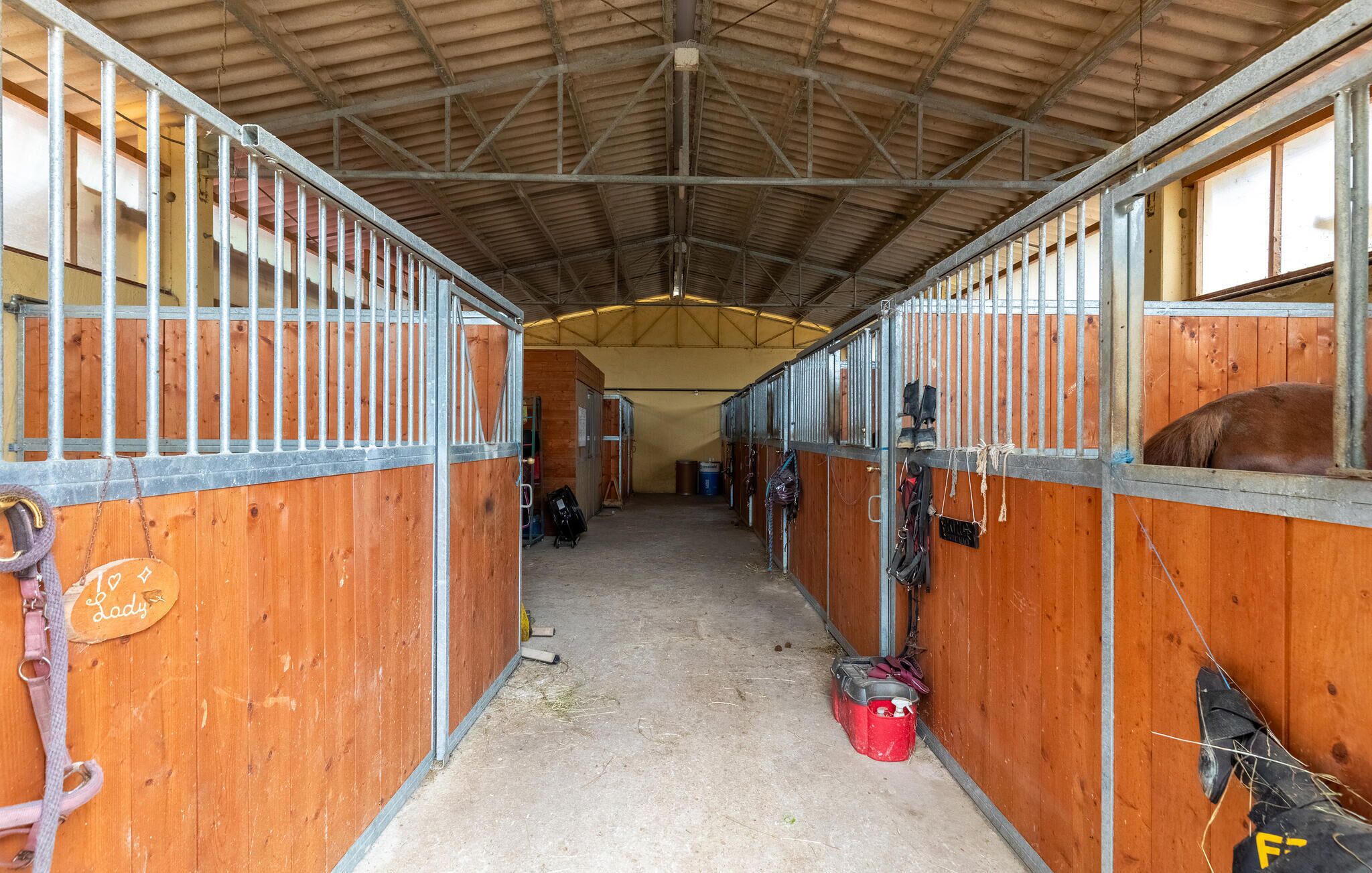 A stable with wooden stalls, metal railings, and a concrete floor.