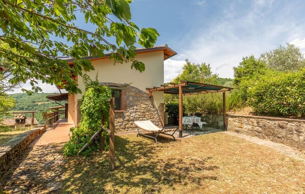 A rustic villa with a stone wall, a pergola, and a dining area with a table and chairs.