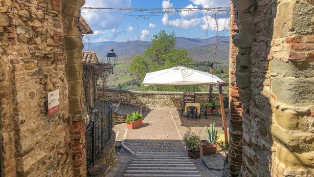 A stone staircase leading to a terrace with a white umbrella, surrounded by stone walls and potted plants.