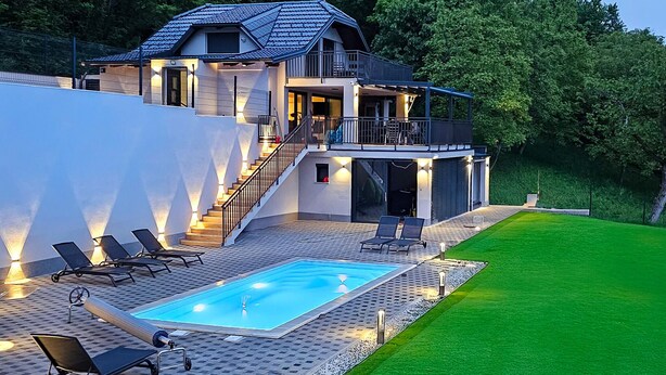Ein modernes, zweistöckiges Haus mit Swimmingpool, Sitzgelegenheiten im Freien und einem gepflegten Rasen.