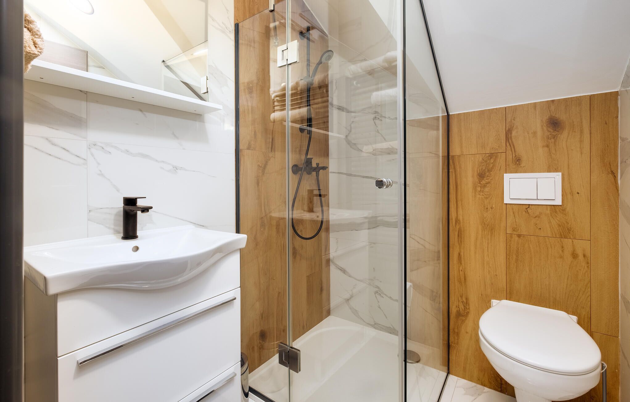 A modern bathroom with a glass-enclosed shower, a white sink, and a toilet.
