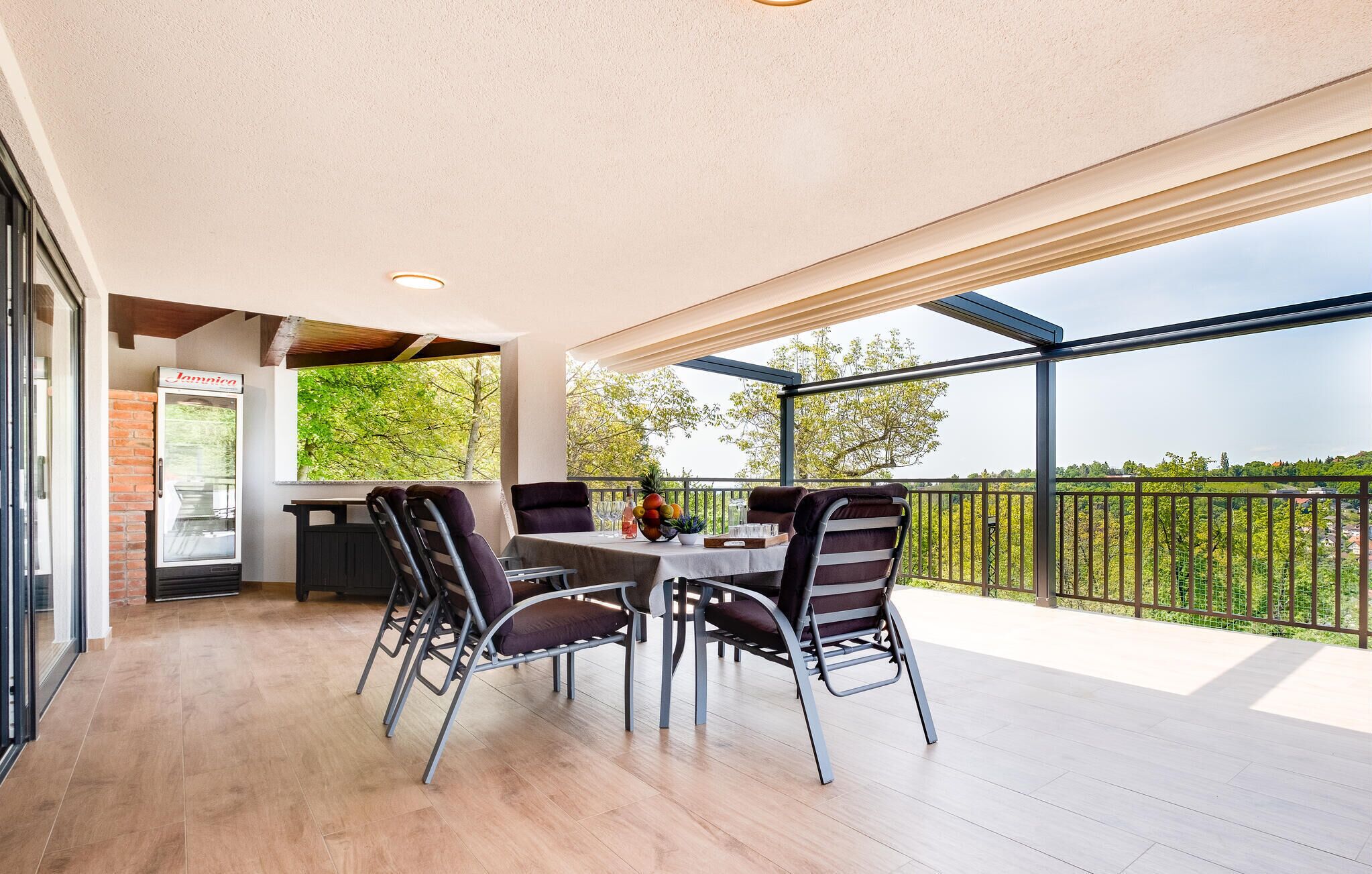 Un balcon avec une table et des chaises, un réfrigérateur et une vue sur la verdure.