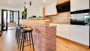Eine moderne Küche mit Kochinsel aus Ziegeln, Barhocker und Holzschränken.