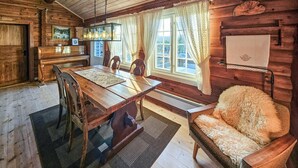 A cozy cabin interior with a wooden dining table, chairs, a fur-covered armchair, a piano, and a large window with curtains. - Stunning home in Flesberg with sauna (Flesberg)