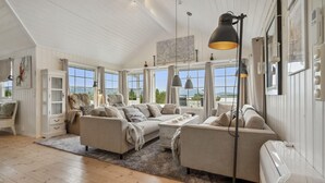A spacious living room with a high ceiling, large windows, and a view of the outdoors. There are multiple seating areas with sofas and a coffee table. - 4 bedroom beautiful home in Lødingen (Lødingen)