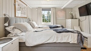 A bedroom with a bed, bedside tables, a dresser, a window with curtains, a wall-mounted TV, and a ceiling light. - 4 bedroom beautiful home in Lødingen (Lødingen)