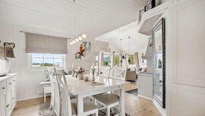 A spacious dining area with a white table and chairs, a large window with a view, and a ceiling with exposed beams. - 4 bedroom beautiful home in Lødingen (Lødingen)