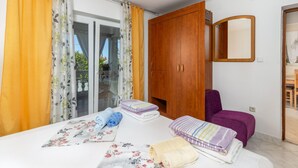 Un dormitorio con cama, armario, una silla morada y un baño visible a través de un cristal.