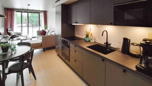 A modern kitchen with a dark countertop, a black sink, and a coffee maker. There is a dining area with a table and chairs, and a sofa in the background.