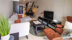 A modern living room with a sofa, coffee table, TV, and a staircase leading to another room.