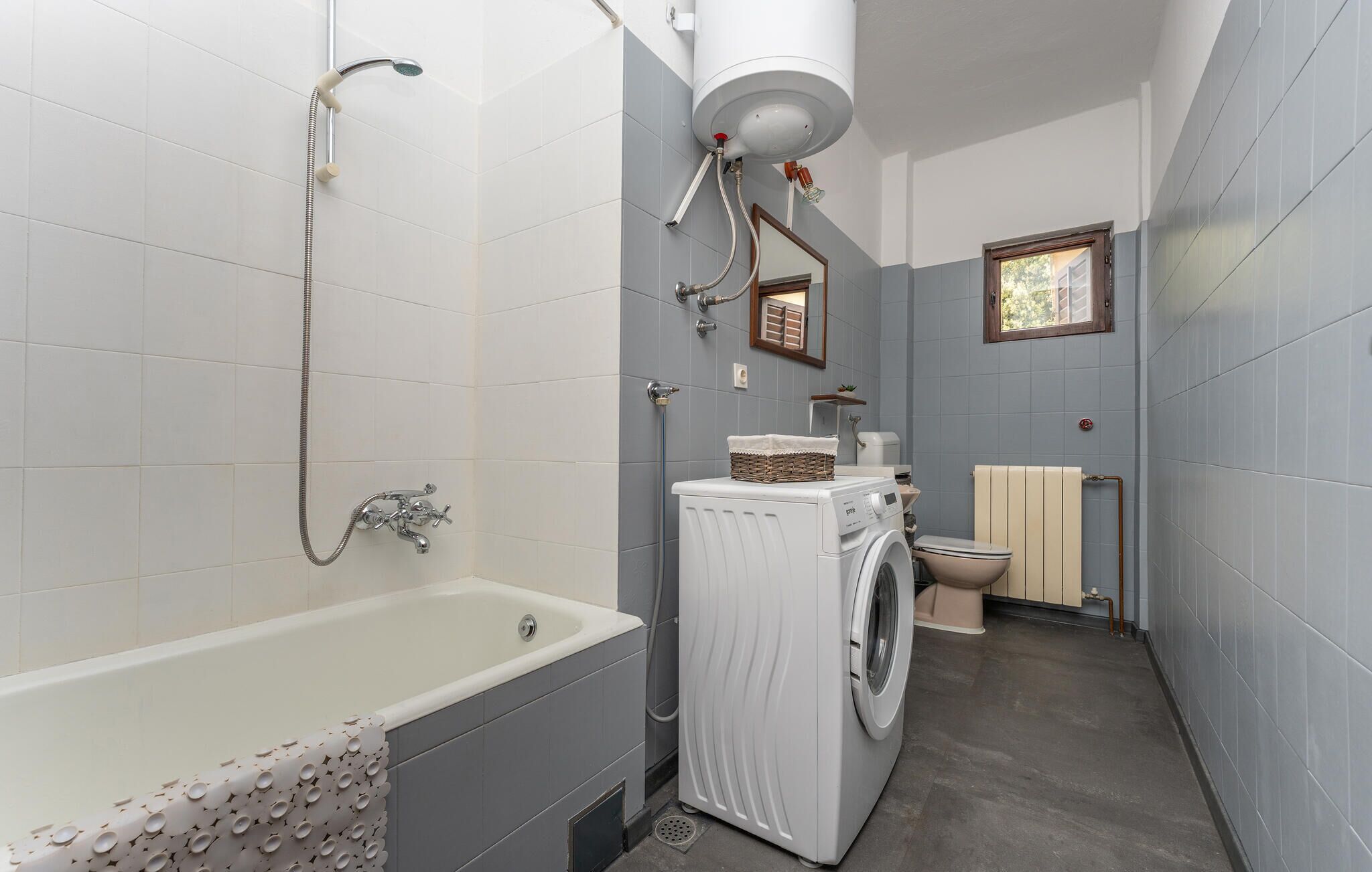 A compact bathroom with a bathtub, a washing machine, a toilet, and a shower.