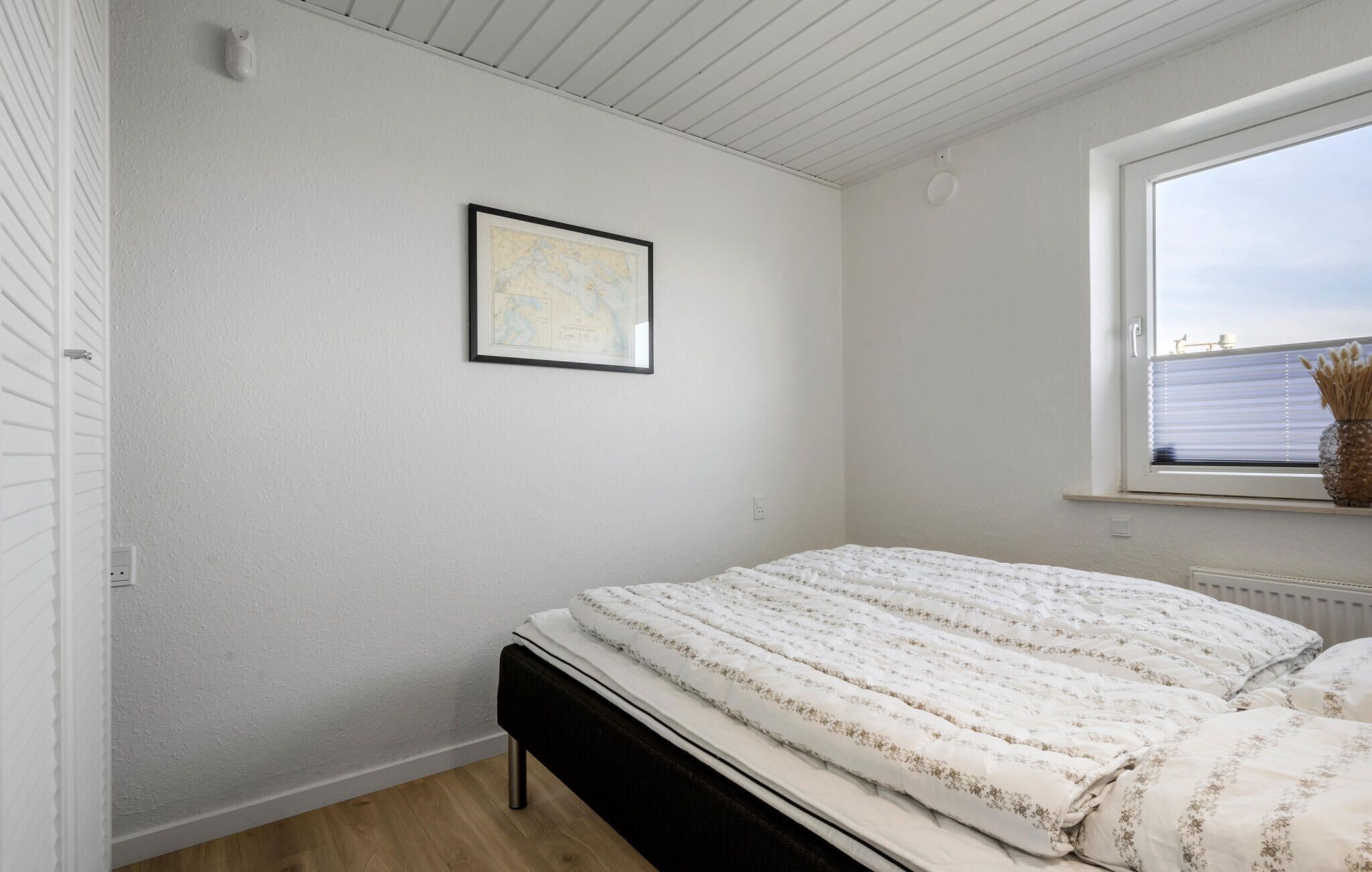 Quarto com cama, um mapa emoldurado na parede e janela com vista.