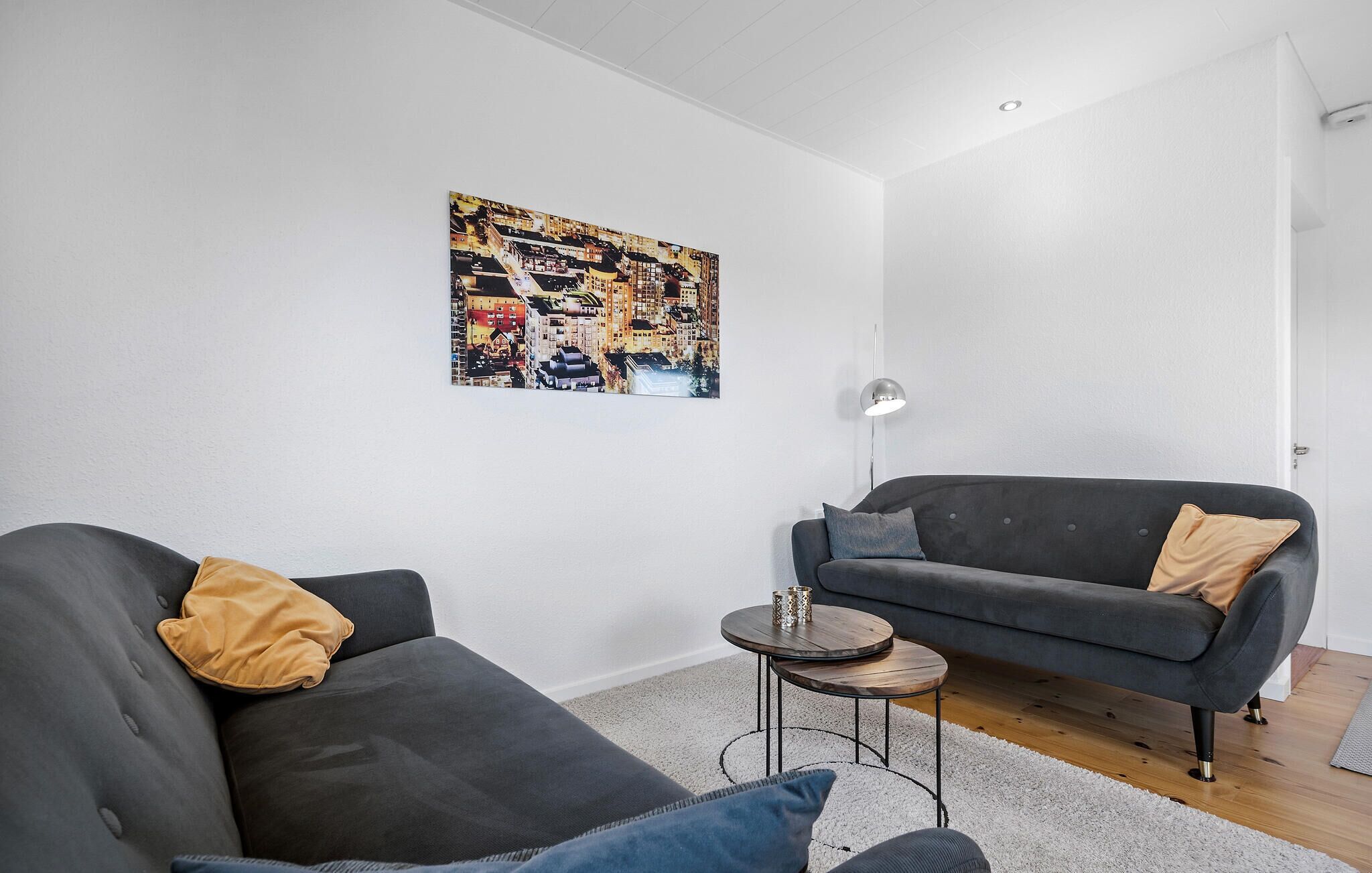 Un salon moderne avec deux canapés gris, une petite table basse ronde et un tableau coloré représentant un paysage urbain accroché au mur.