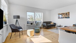 A modern living room with a large window, a floor lamp, a sofa, a chair, a round table, and a radiator. - 2 bedroom amazing home in Ringkøbing (Ringkøbing)