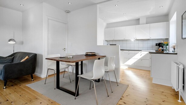 A modern kitchen with white cabinets and a wooden dining table. - 2 bedroom amazing home in Ringkøbing (Ringkøbing)