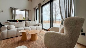Una sala de estar moderna con un sofá, dos mesas auxiliares de madera y un sillón mullido.