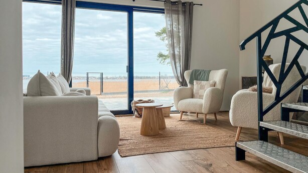 Un salón amplio con un ventanal grande, dos sofás, una mesa de centro y una escalera con barandilla geométrica.
