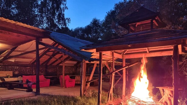A rustic outdoor seating area with a fire pit under a metal roof structure. - Cozy home in Plock with house a panoramic view (Plock)