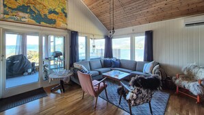 Un salón amplio con un gran ventanal con vistas panorámicas, techo de madera y un rincón de descanso acogedor.