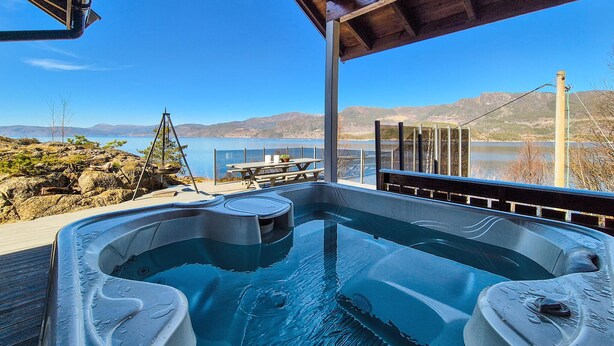 Un jacuzzi con muelle de madera y vistas a un lago y montañas.