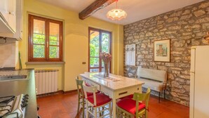 A kitchen with a stone wall, a dining table with chairs, a radiator, and a window with a view of greenery. - Nice home in Monte S.Maria Tiberina (Monte S.Maria Tiberina)