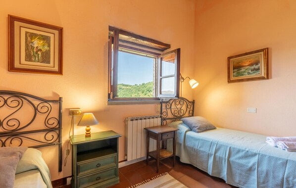 Une petite chambre à coucher, chaleureuse et accueillante, avec un lit simple, une table de chevet, une lampe et une fenêtre donnant sur un paysage verdoyant.