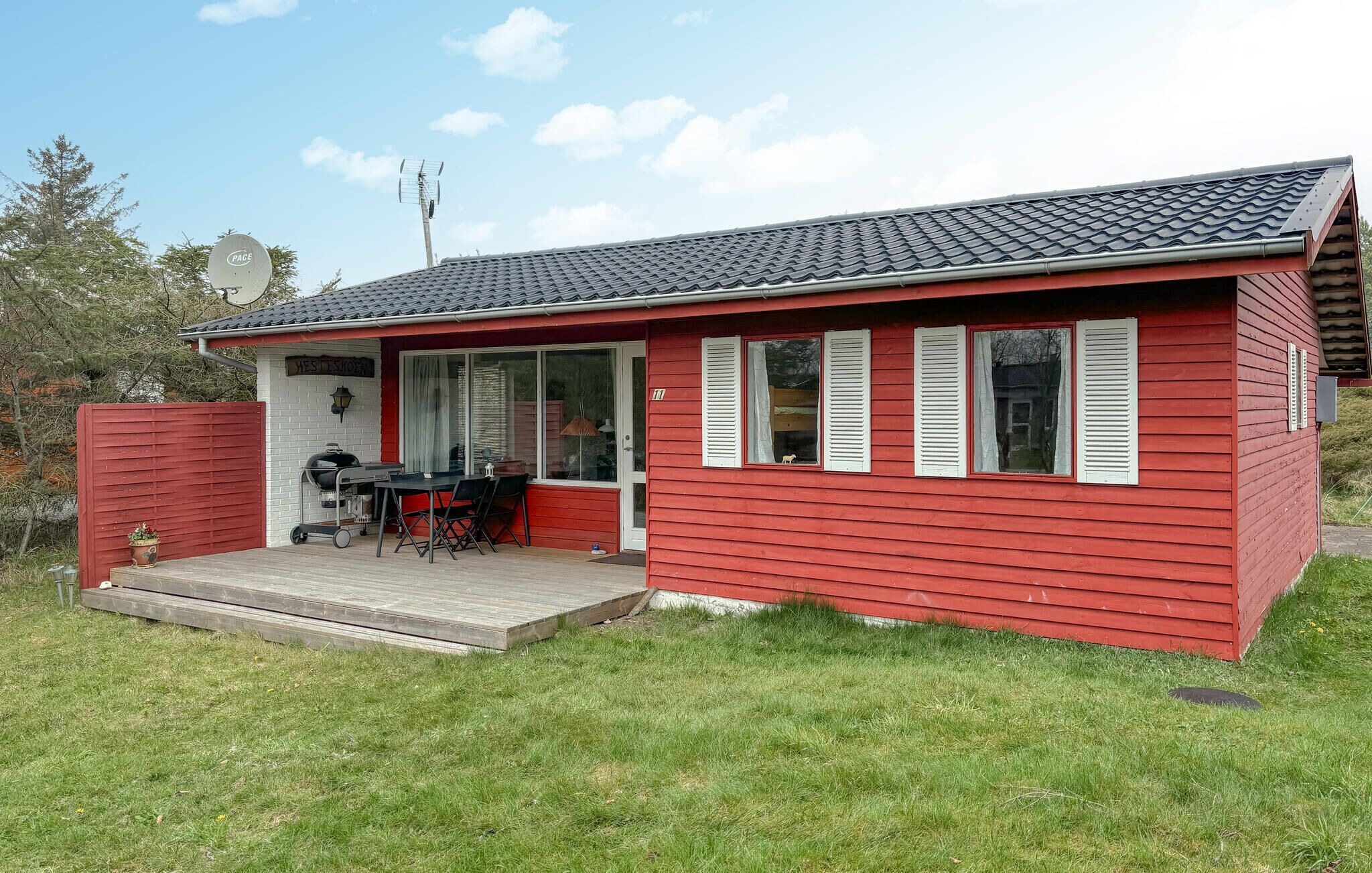 Une petite maison rouge avec un porche abrité, un barbecue et une enseigne sur laquelle on peut lire « Pace ».