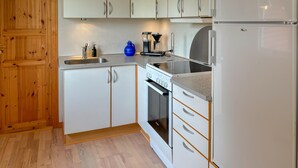 A modern kitchen with white cabinets, a built-in oven, a coffee maker, and a refrigerator.