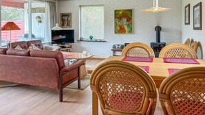 A cozy living room with a brown sofa, a TV, and a dining area with wicker chairs and a wooden table.