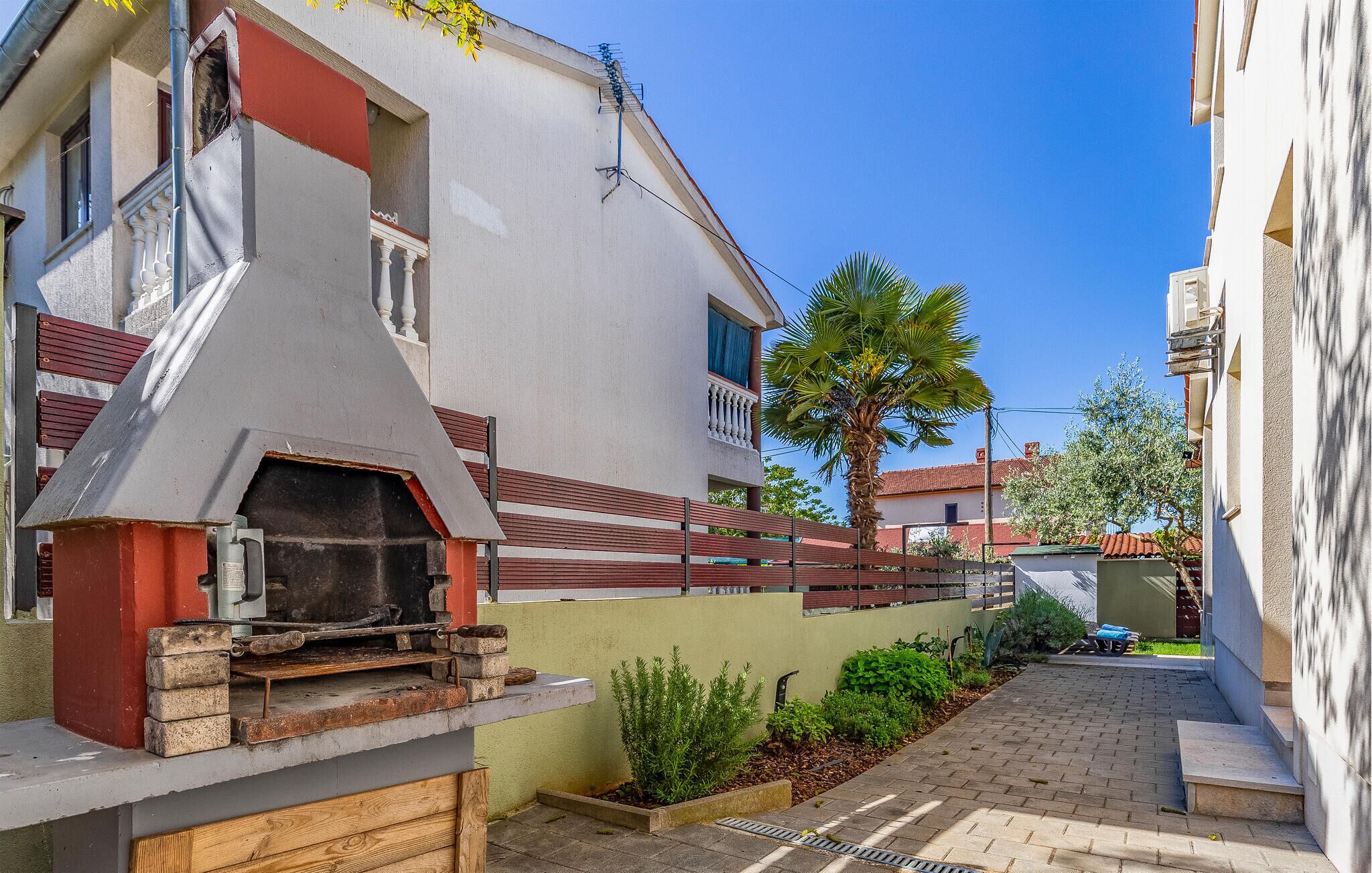Une rue étroite avec un barbecue et un petit espace jardin.