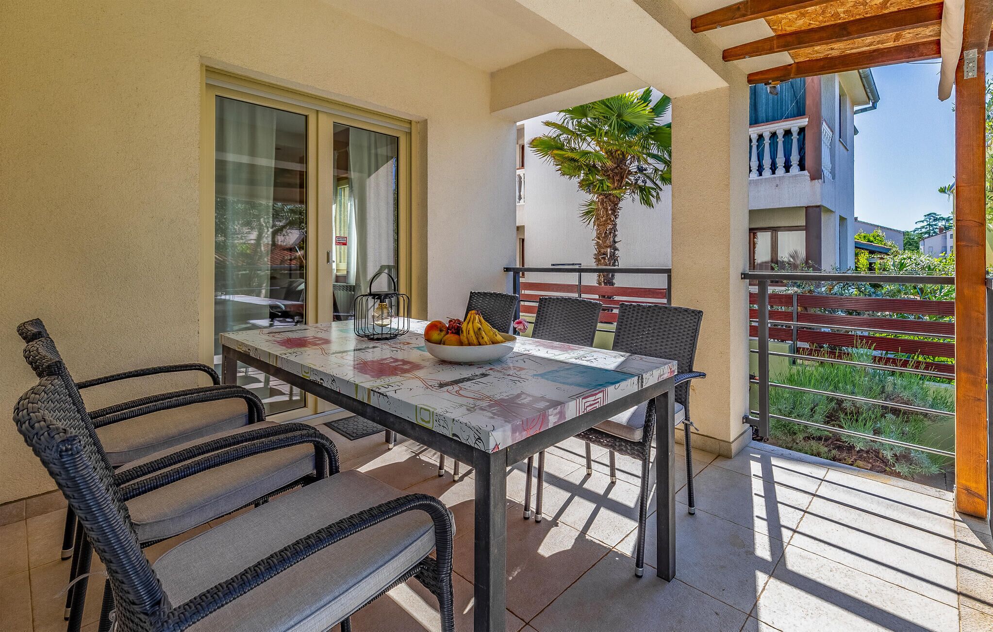 A balcony with a table and chairs, a bowl of fruit, and a potted plant.