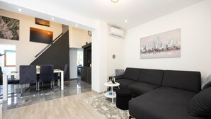 A modern living area with a black sofa, a dining table with chairs, a staircase, and a cityscape painting on the wall. - Gorgeous home in Kricke (Kricke)