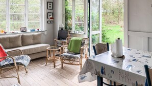 A cozy room with a sofa, wicker chairs, a dining table with a tablecloth, and large windows offering a view of greenery. - Cozy home in Knebel with WiFi (Knebel)