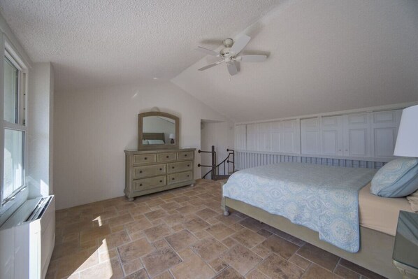 A bedroom with a bed, dresser, mirror, ceiling fan, and radiator.
