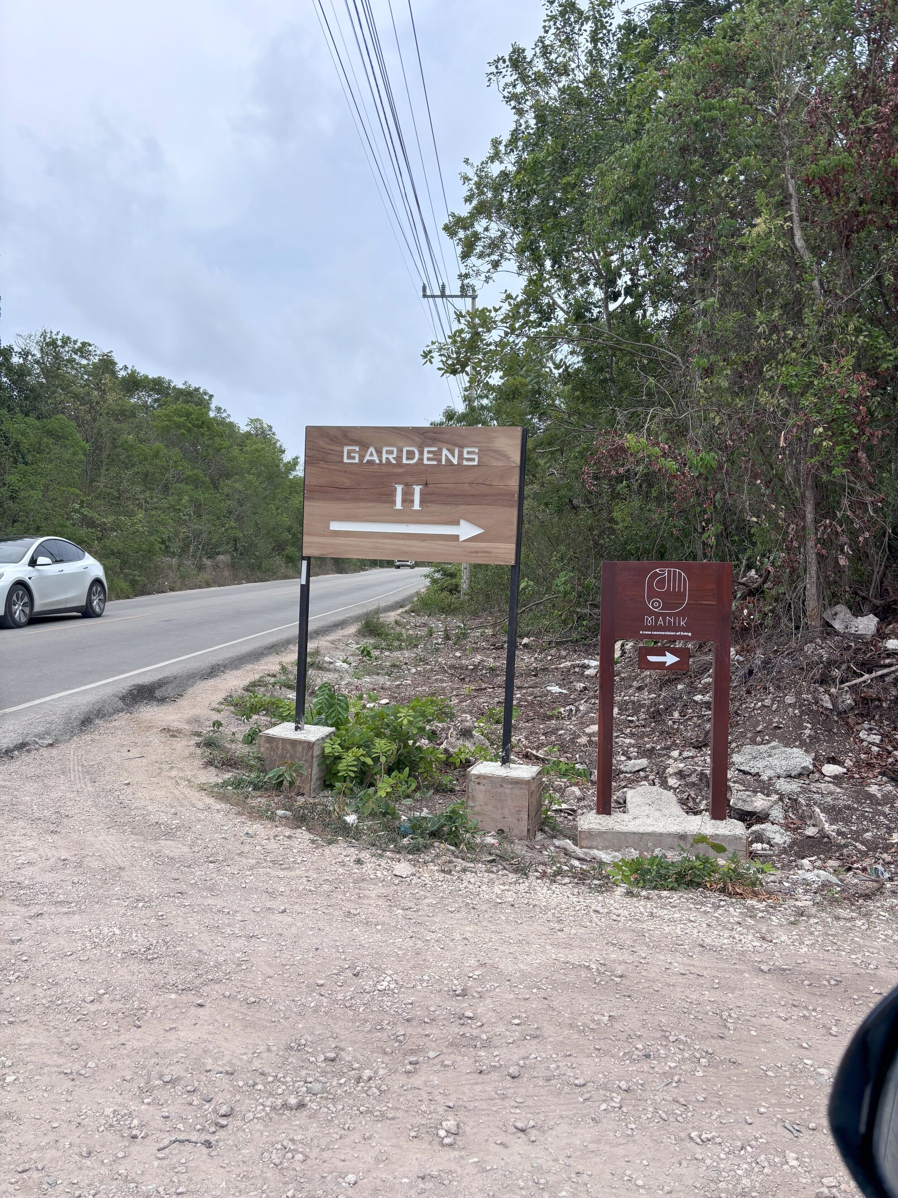 A sign for 'Gardens II' with an arrow pointing right, and a smaller sign for 'Manik' with an arrow pointing left.