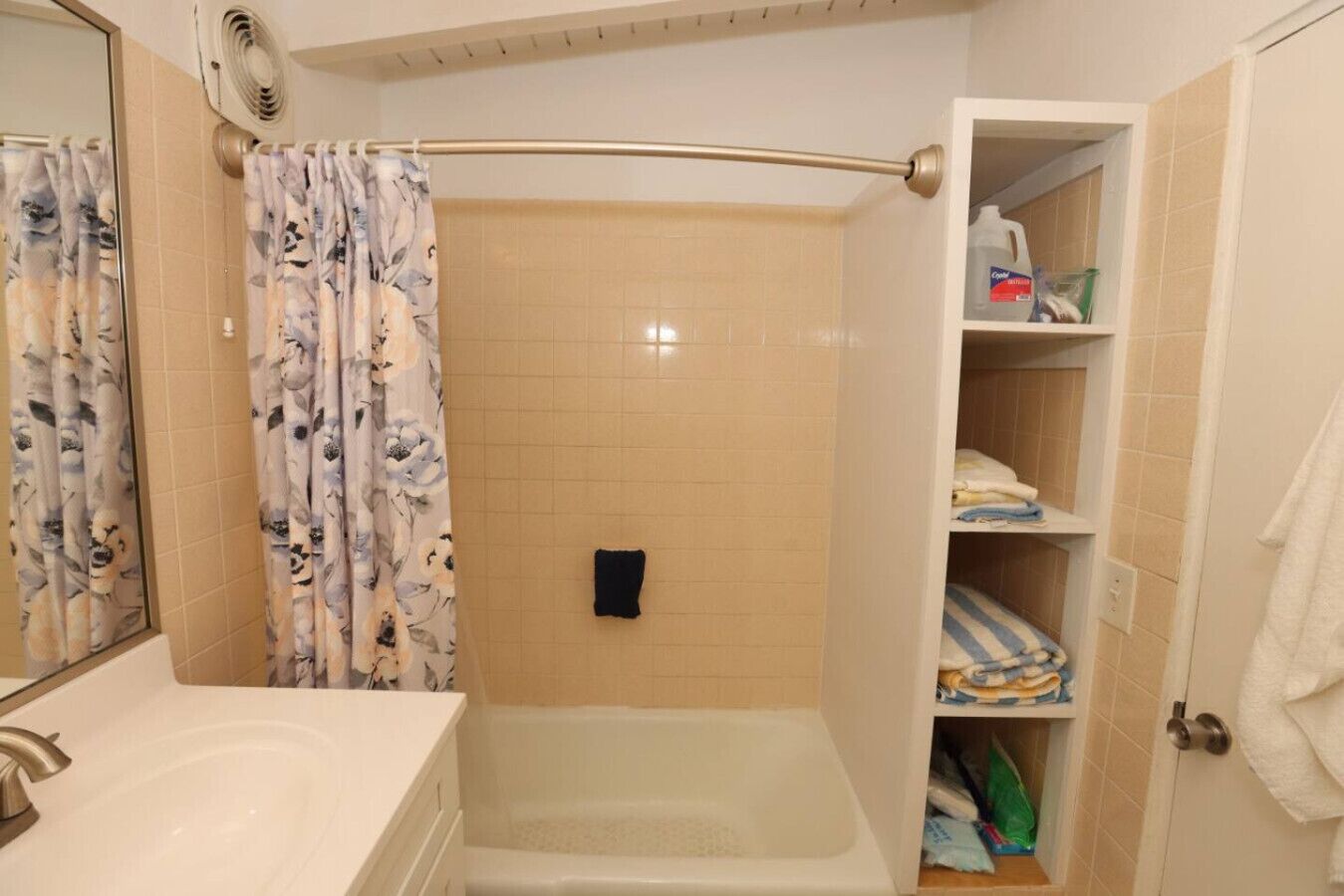 A bathroom with a bathtub, a shower curtain, a towel rack, and a shelf with toiletries.