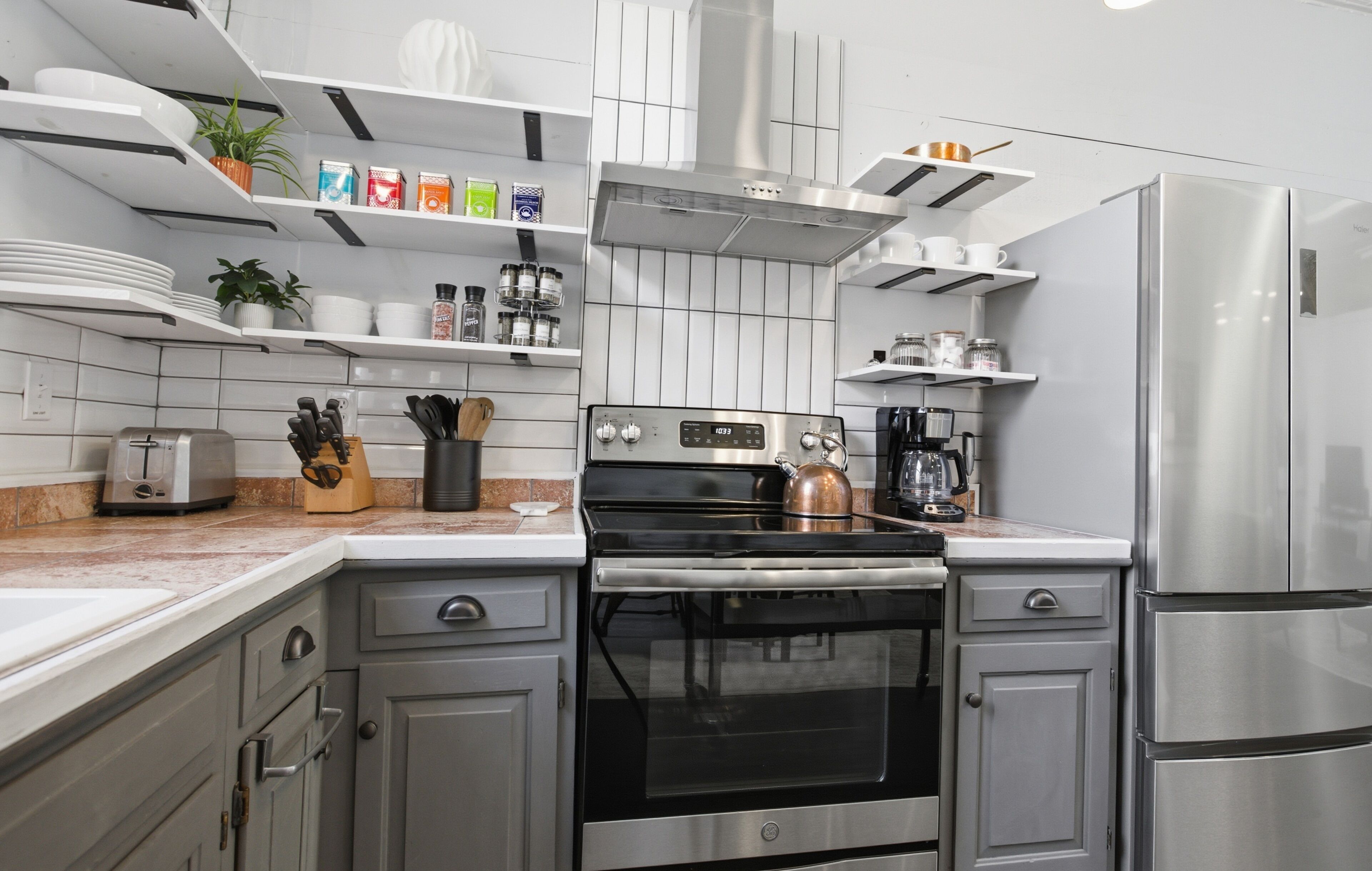 Una cucina moderna con elettrodomestici in acciaio inossidabile, mobili bianchi e una varietà di utensili da cucina sugli scaffali.