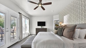 A bedroom with a bed, a ceiling fan, a TV, and a view of the outdoors. - Hillside Harmony Luxury Comfort (Boise)