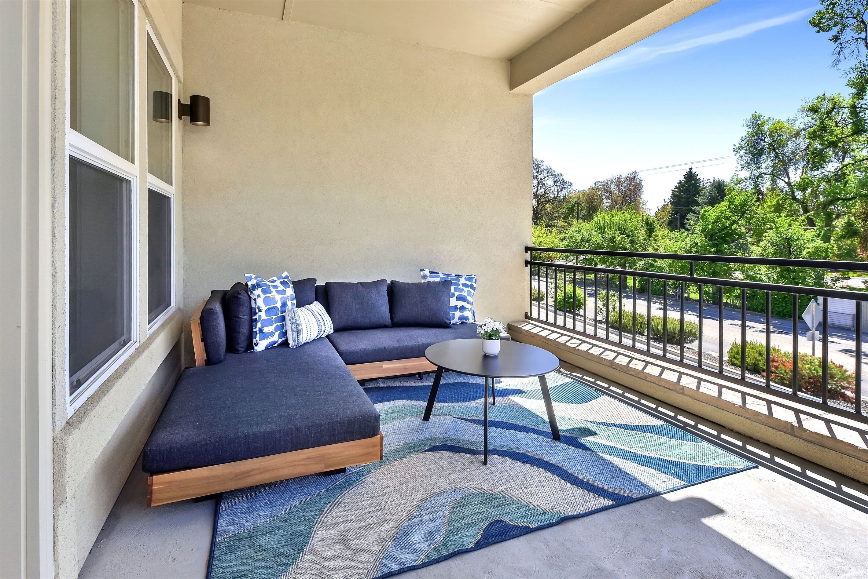 A balcony with a dark-colored sofa, a small round table, and a patterned rug.