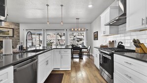 A modern kitchen with white cabinetry, a central island, stainless steel appliances, and a stone backsplash. - Hillside Harmony Luxury Comfort (Boise)