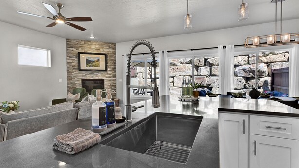 A modern kitchen with a central island, white cabinetry, a stone accent wall, and a view of the outdoors. - Hillside Harmony Luxury Comfort (Boise)