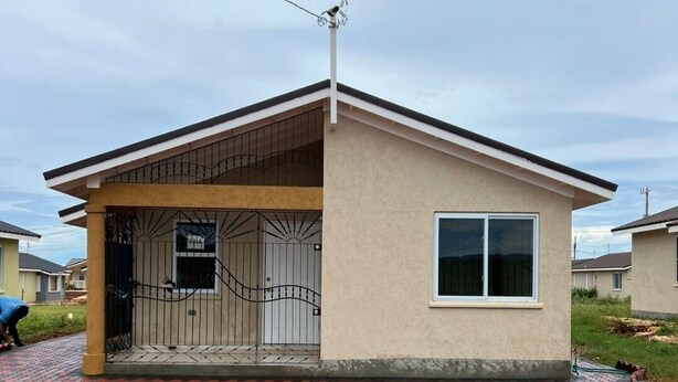 Una pequeña casa de un piso con techo plano, un porche delantero y una reja de metal.