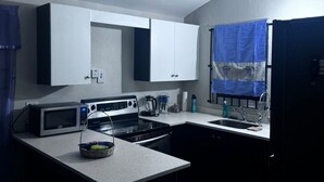 Una cocina compacta con armarios blancos, un microondas, estufa y lavaplatos.