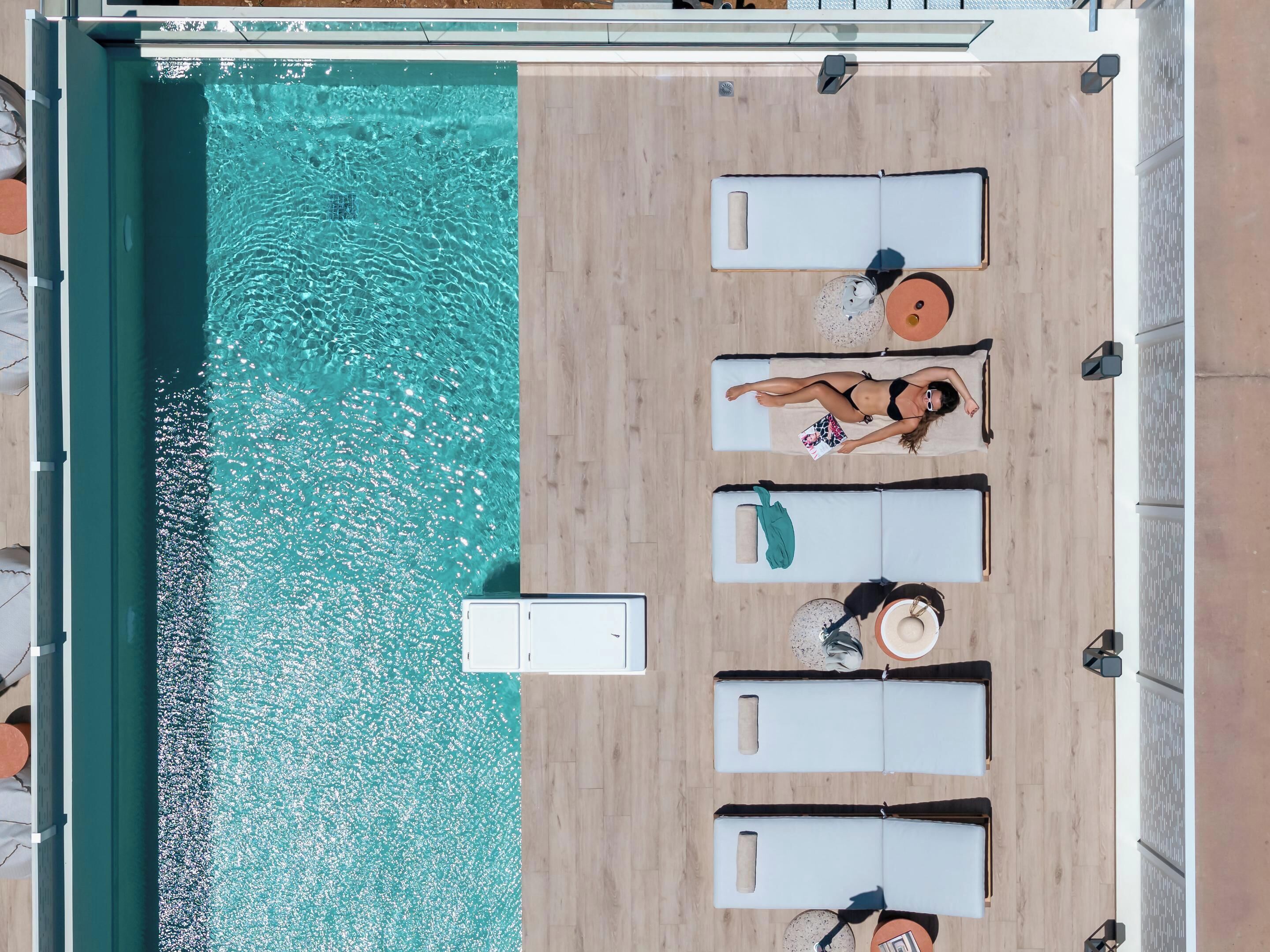 An aerial view of a pool area with four sun loungers, a small table, and a chair.