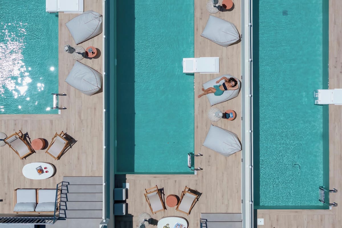 An aerial view of a pool area with multiple lounge chairs, sunbeds, and a central walkway.