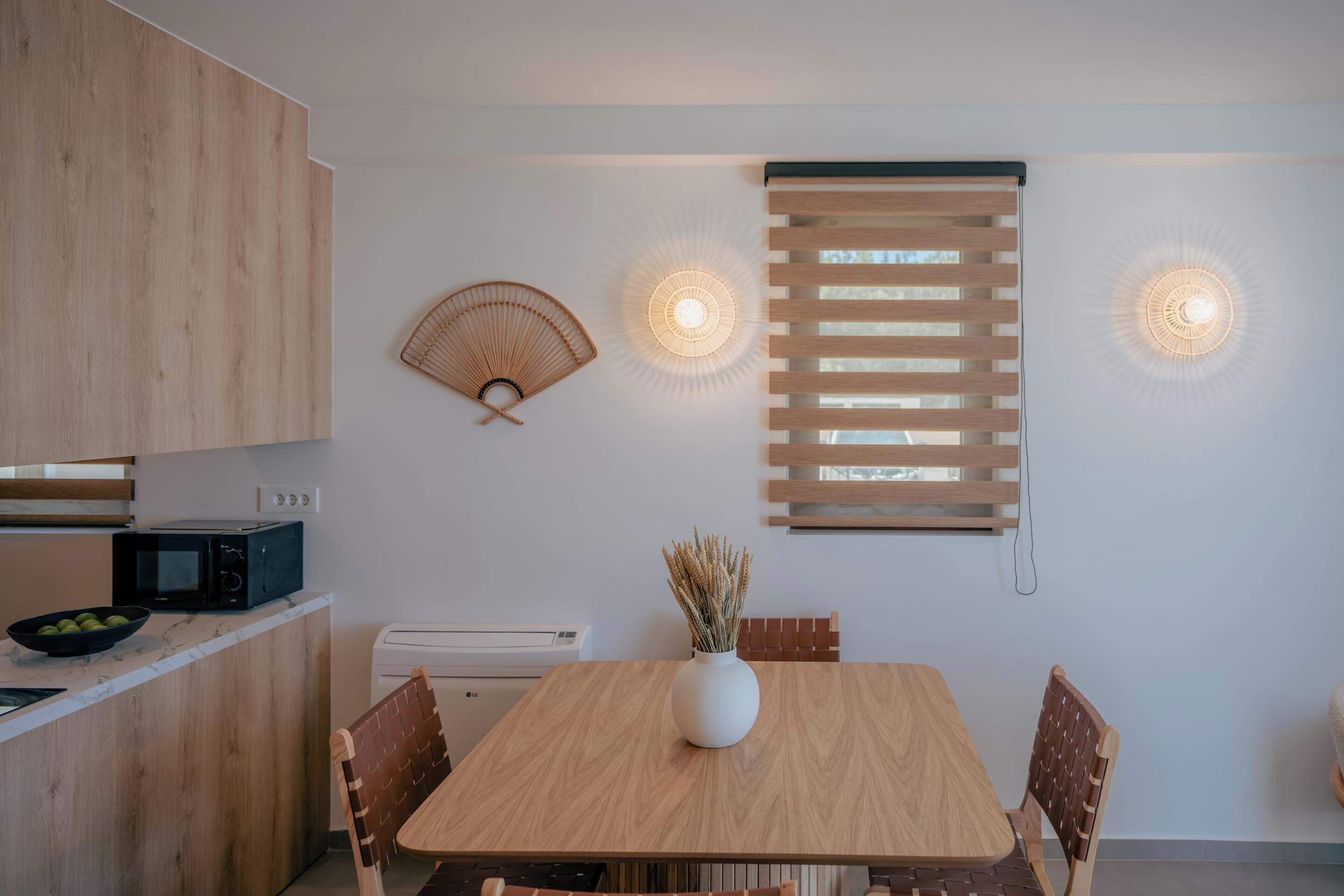 Une cuisine moderne avec une table en bois, des chaises, un four à micro-ondes et un saladier rempli de fruits.