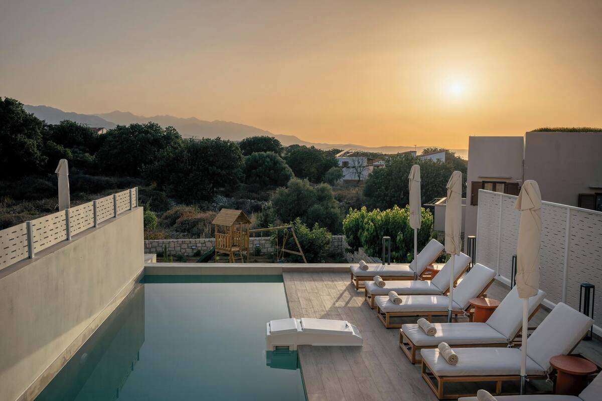 A rooftop pool area with lounge chairs and a wooden playhouse, overlooking a mountainous landscape.